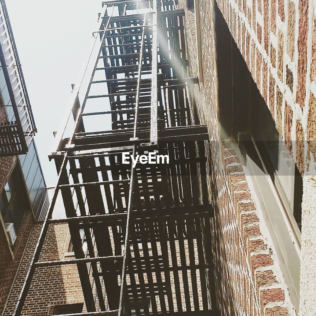 Low angle view of fire escape ladder on apartment building against sky