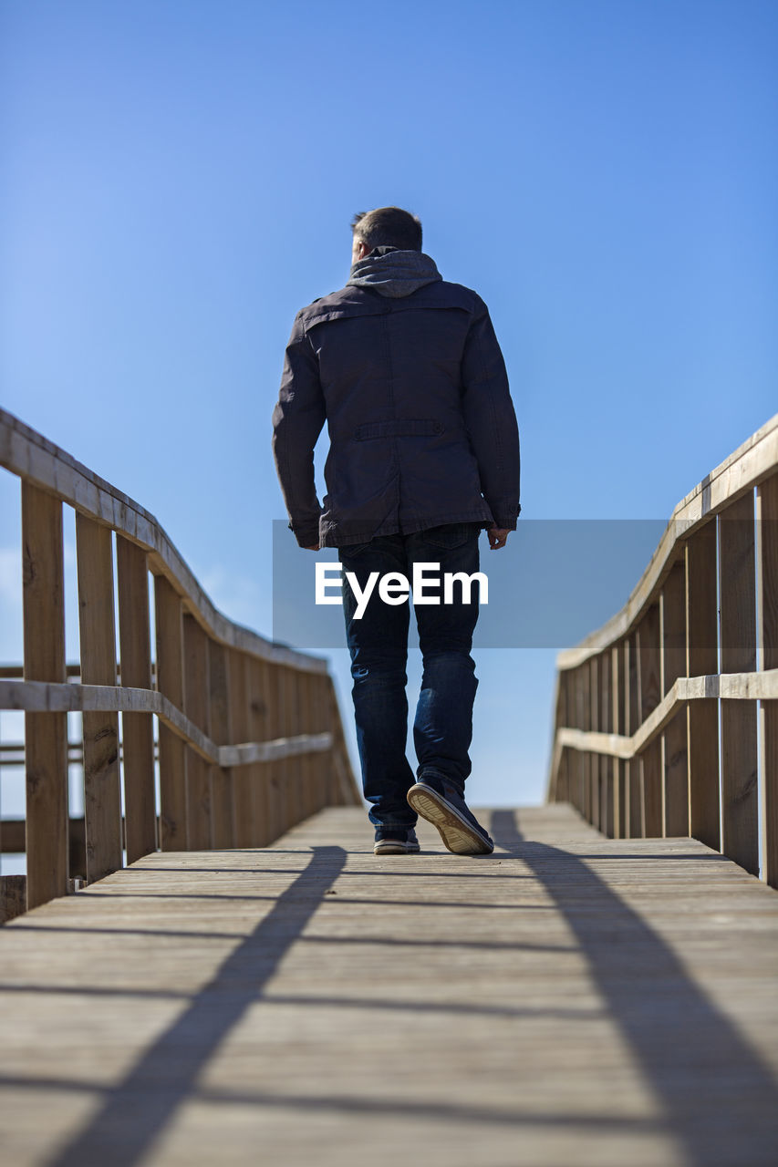 FULL LENGTH REAR VIEW OF MAN STANDING ON FOOTBRIDGE