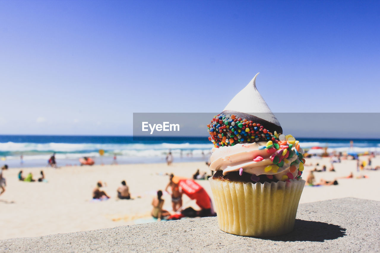 Close-up of cupcake on beach against clear blue sky