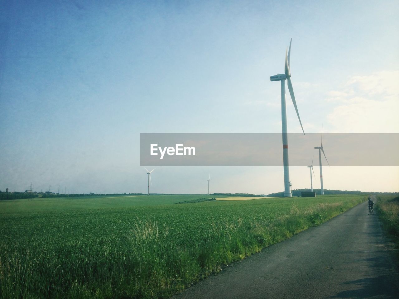 Wind turbines on landscape along empty road against sky