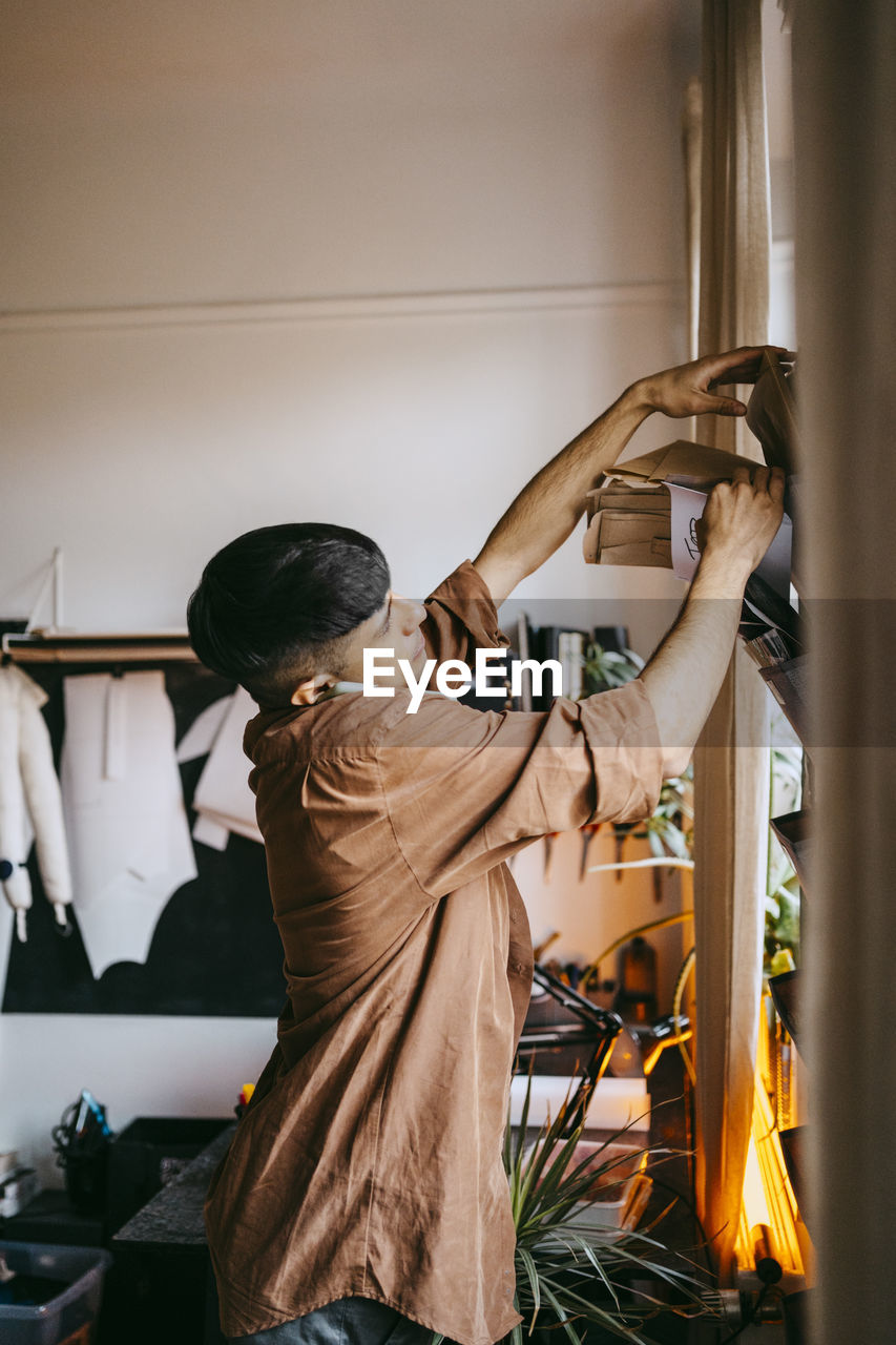 Side view of businessman talking on smart phone and removing reminders from rack at home office