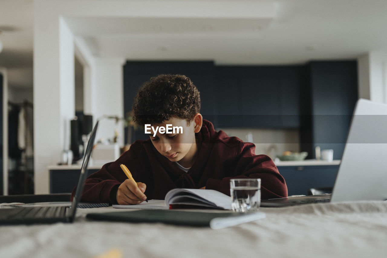 Boy doing homework while sitting near table at home