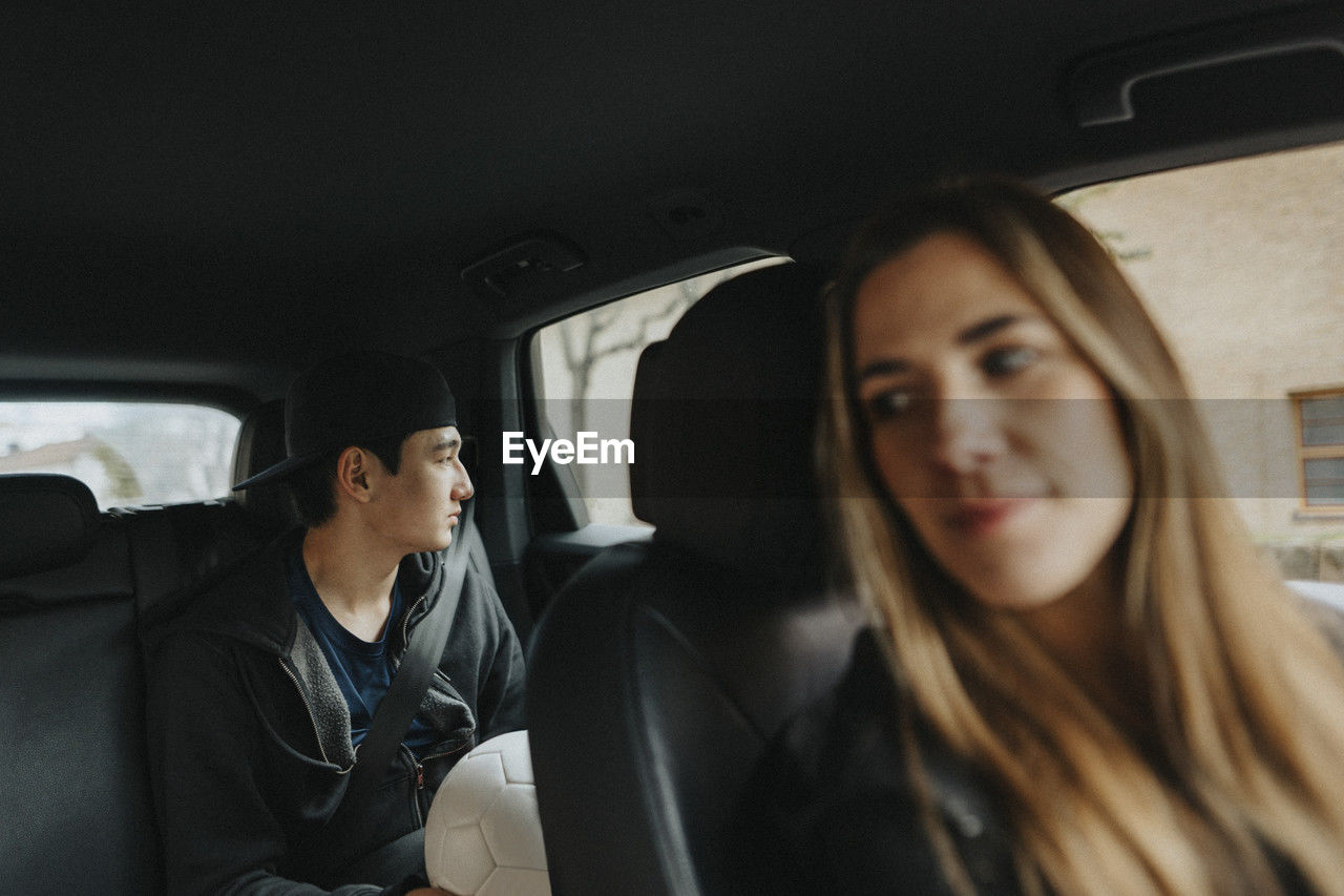Contemplative teenage boy sitting with female coach in car