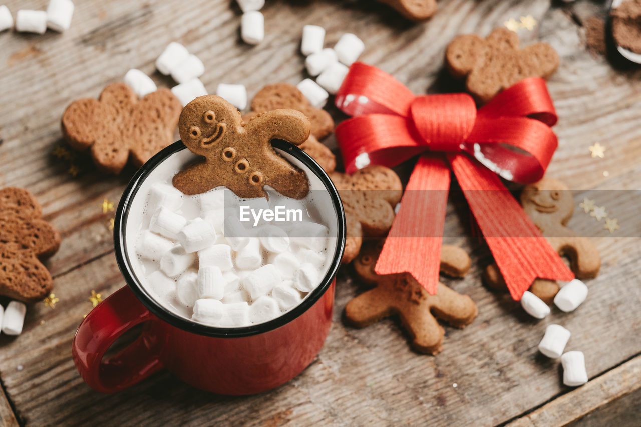 Ginger man in a cup of cocoa with a big red bow on a wooden background, top view. 