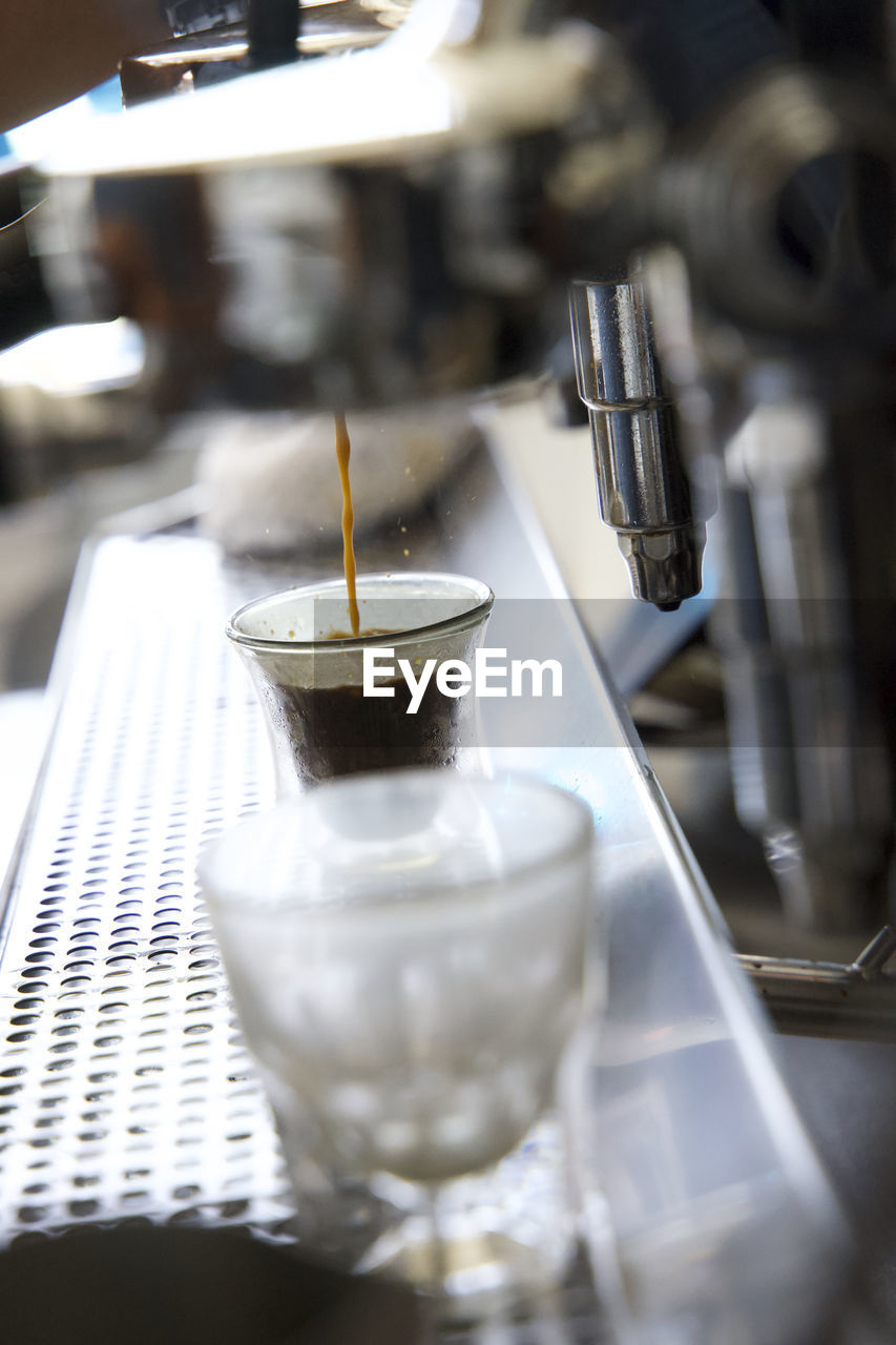 Close up of espresso maker pouring espresso into a small glass in a coffee shop