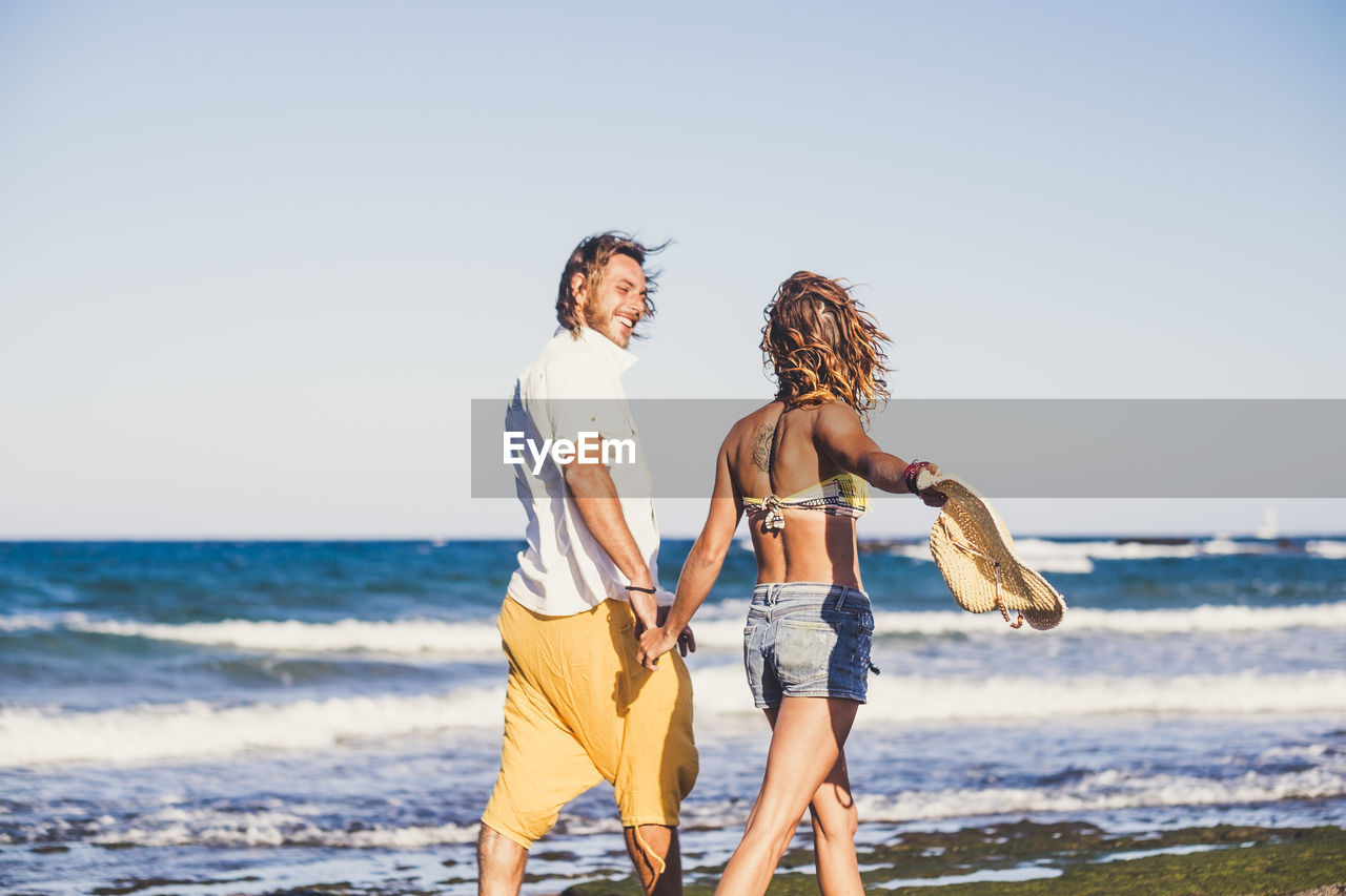 Couple walking at beach against sky
