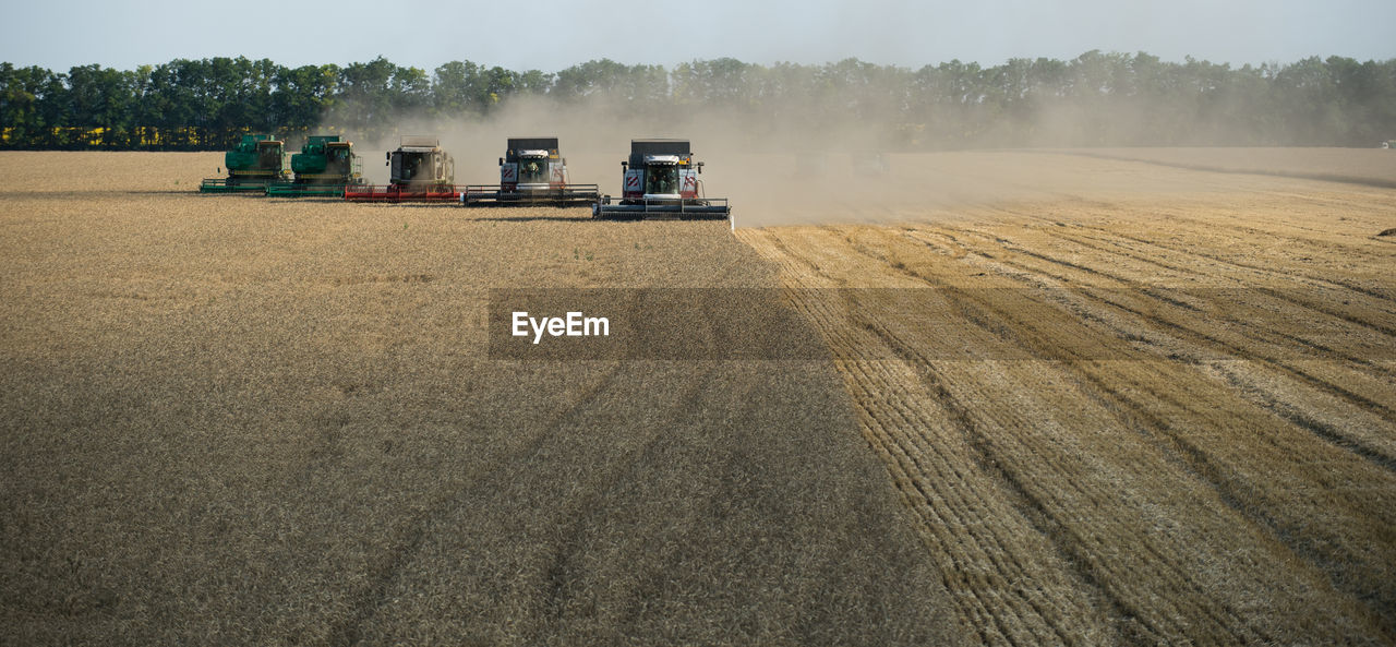 Combine harvester on field against sky at farm during sunset