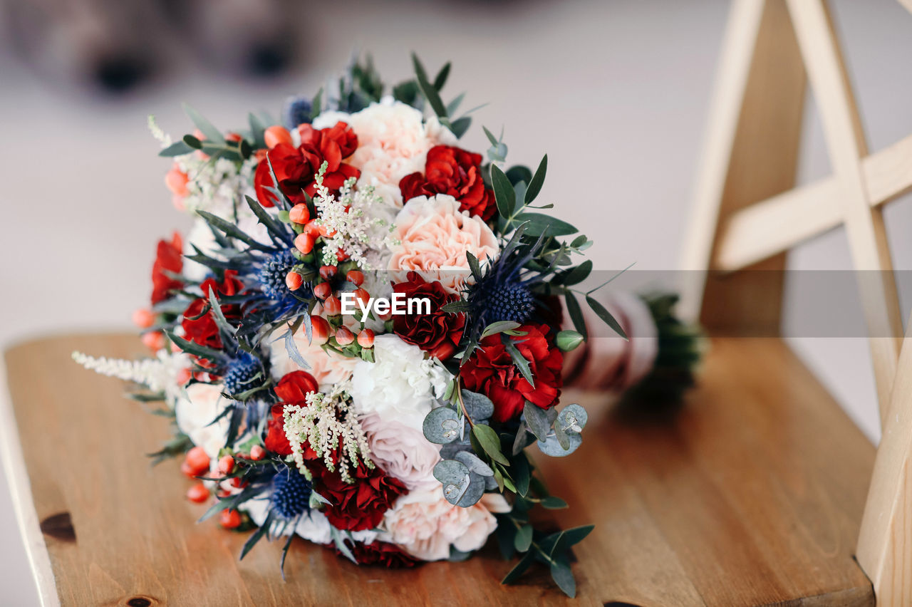 A bride with a wedding bouquet of roses and carnations on the background of a wedding dress