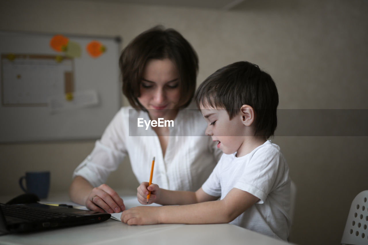 Tutor deals with the preschooler with a laptop, a real home interior, the concept of childhood