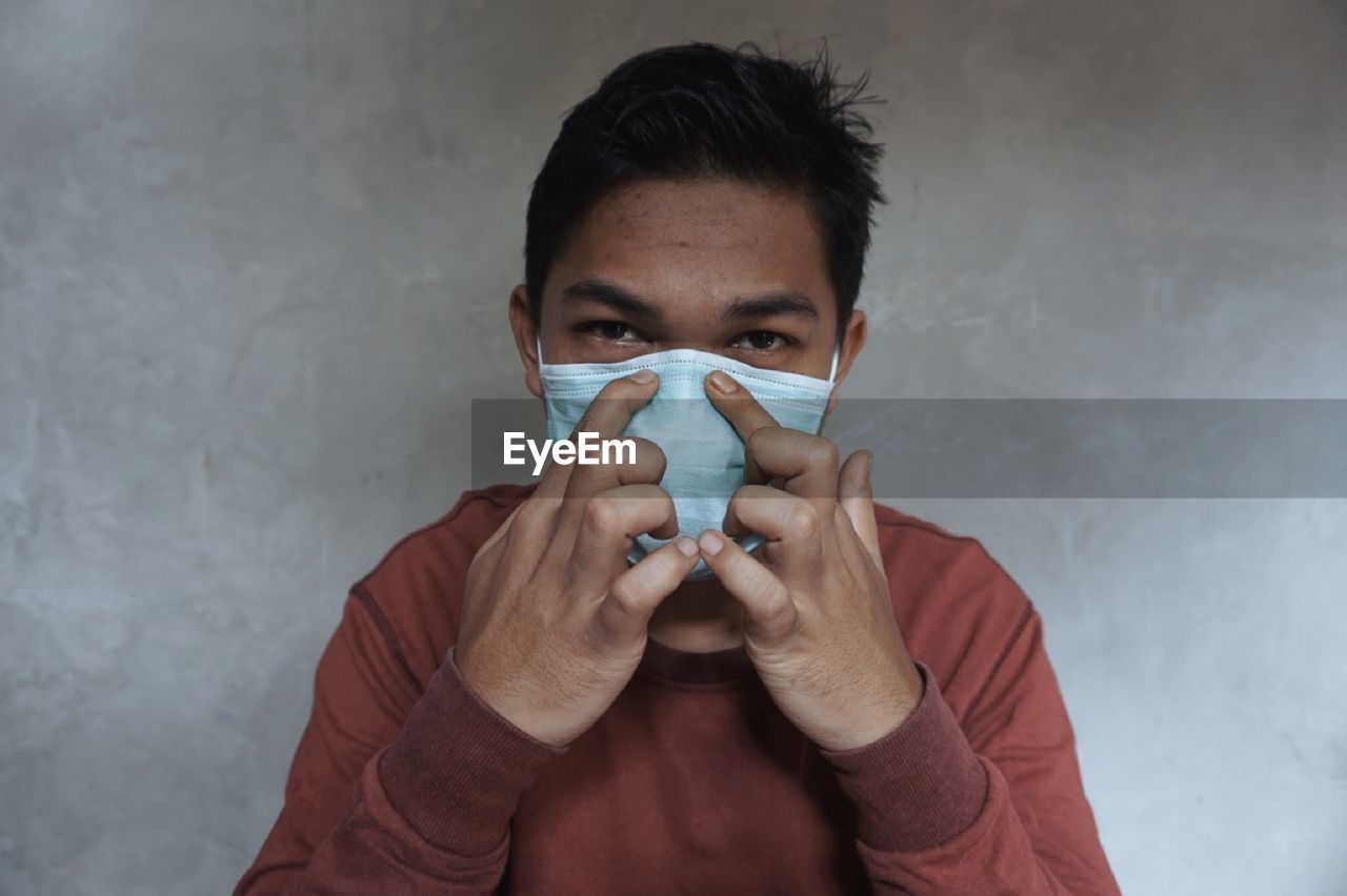 Portrait of young man holding eyeglasses against wall