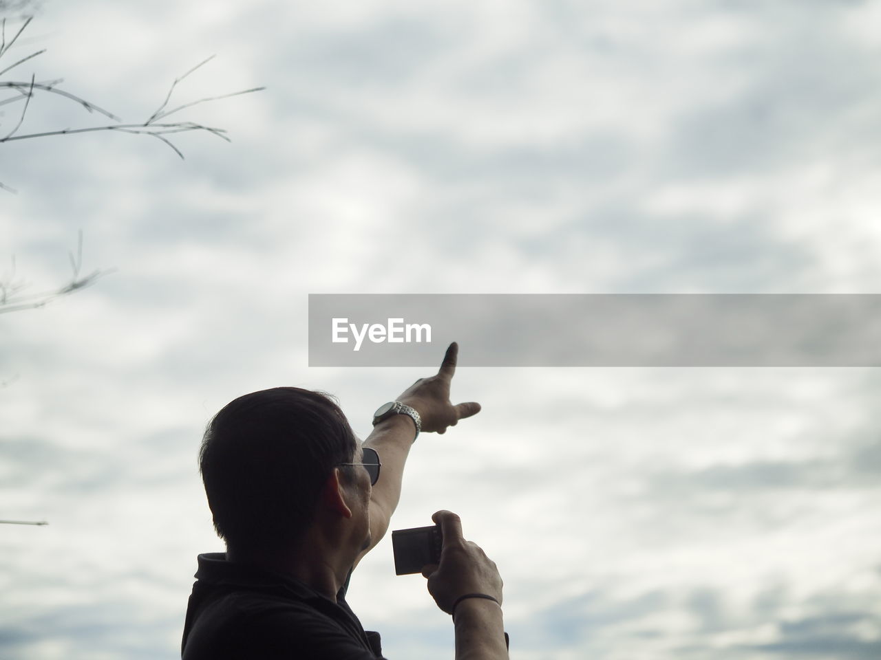 Low angle view of man holding camera while showing cloudy sky