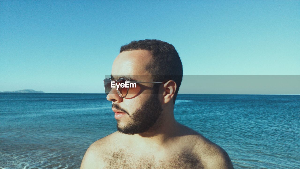 Close-up of young man wearing sunglasses at beach against clear sky
