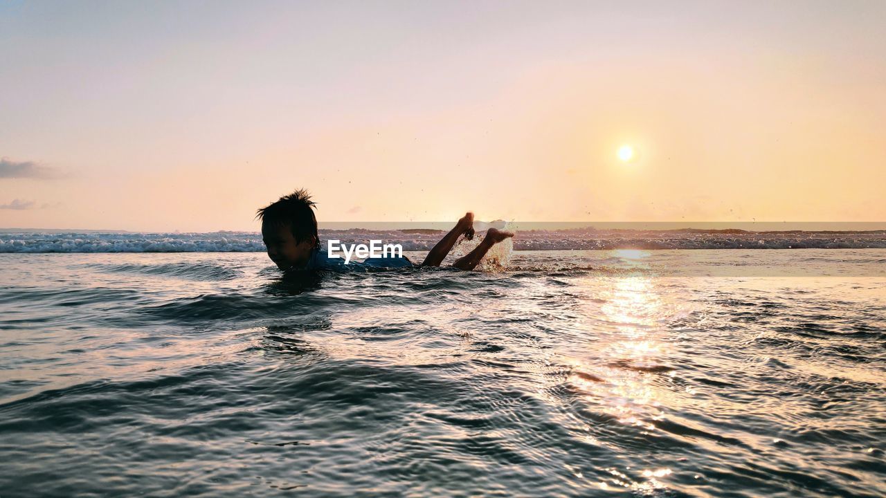 People swimming in sea against sky during sunset