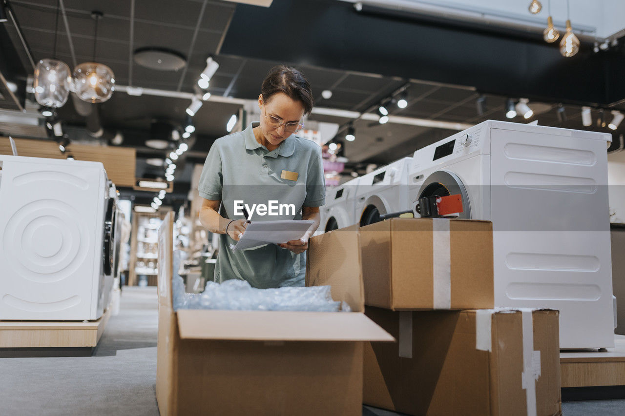 Female writing in document over open cardboard box while working in appliances store