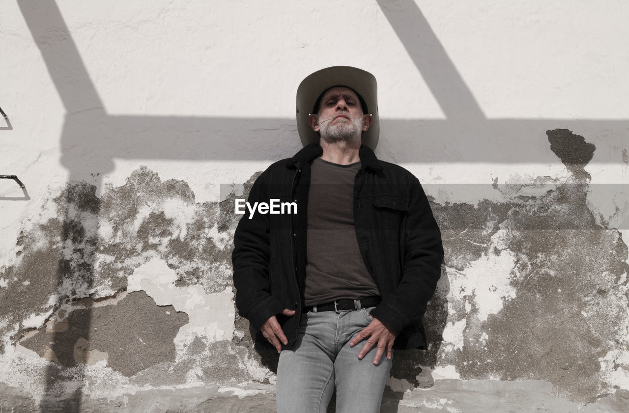 Portrait of adult man in cowboy hat and jeans against wall with sunlight and shadow. almeria, spain