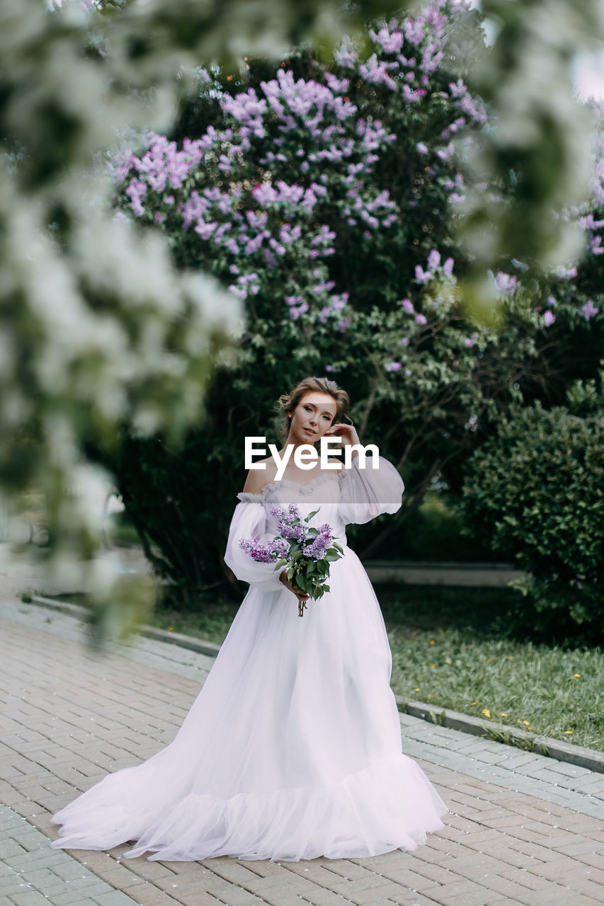 Beautiful bride in a wedding dress walks in a blooming apple-tree park in spring