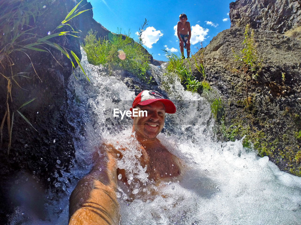 Smiling man in waterfall with boy in background