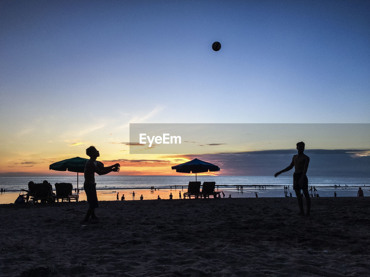 Silhouette people playing with ball at beach against sky during sunset