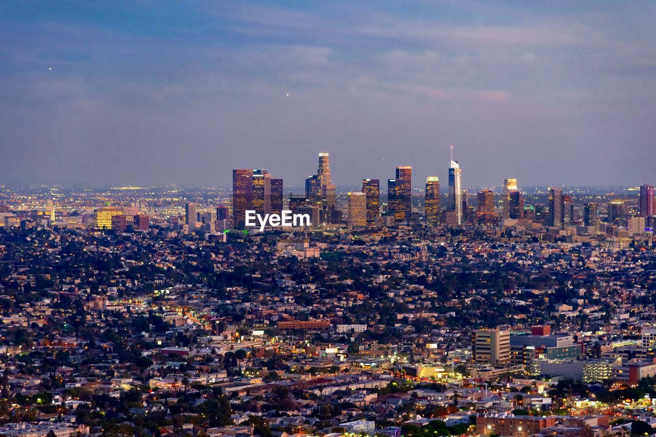 Aerial view of buildings in city against cloudy sky