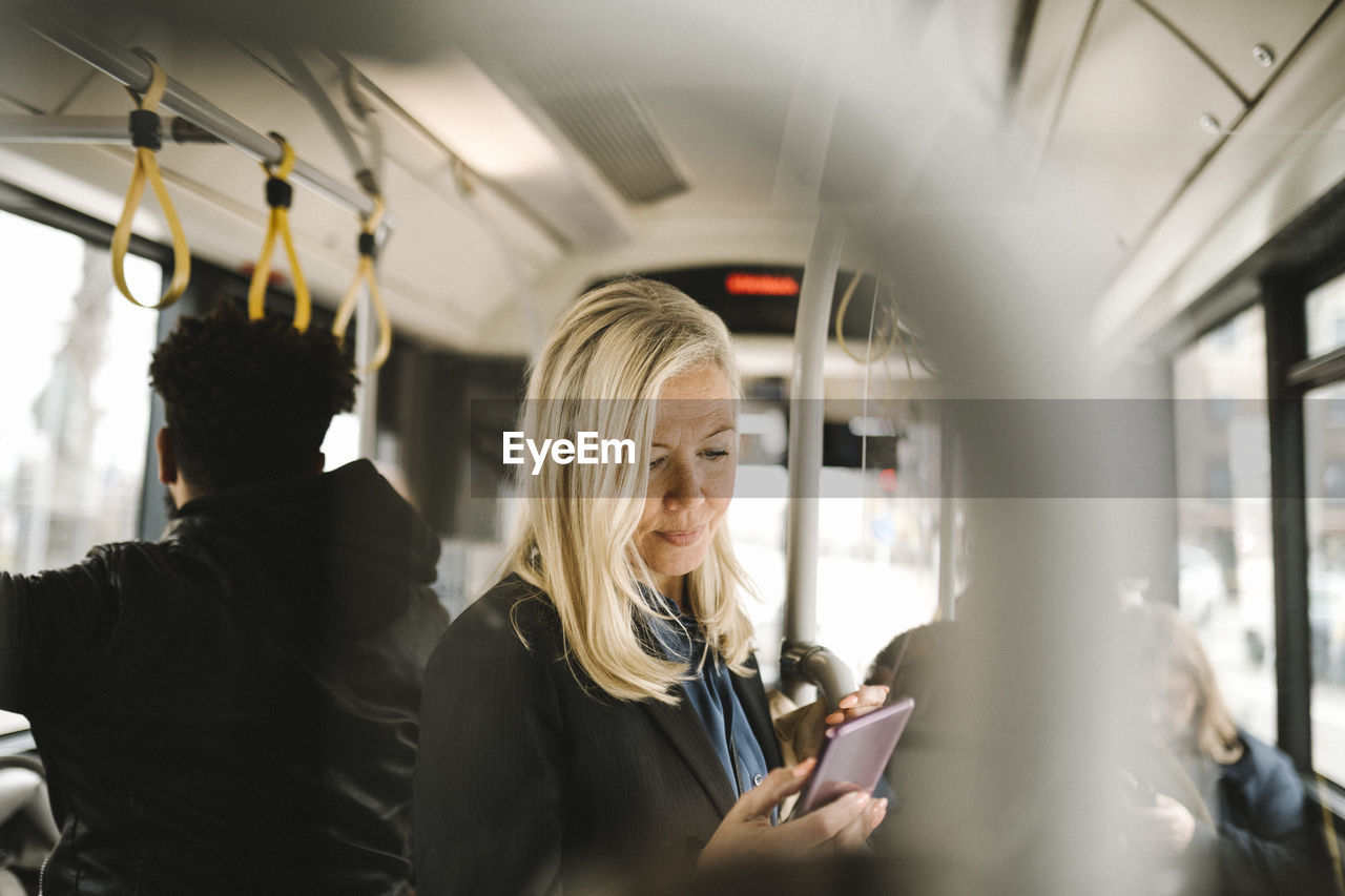 Female professional using smart phone while standing in bus