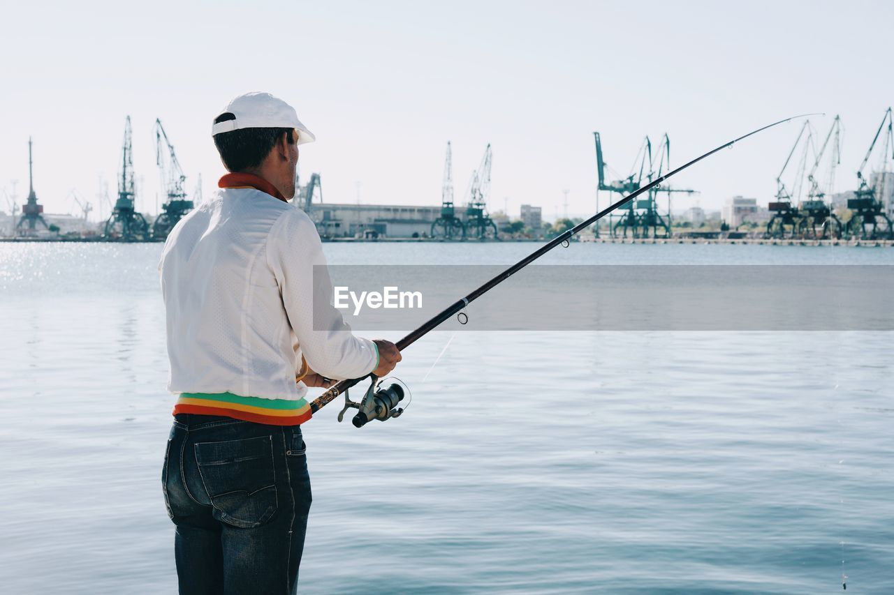 Rear view of man fishing at harbor