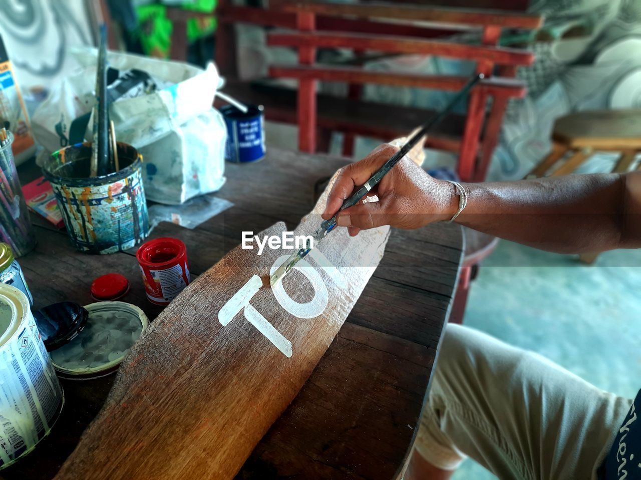 Midsection of man writing text on wooden plank with paint