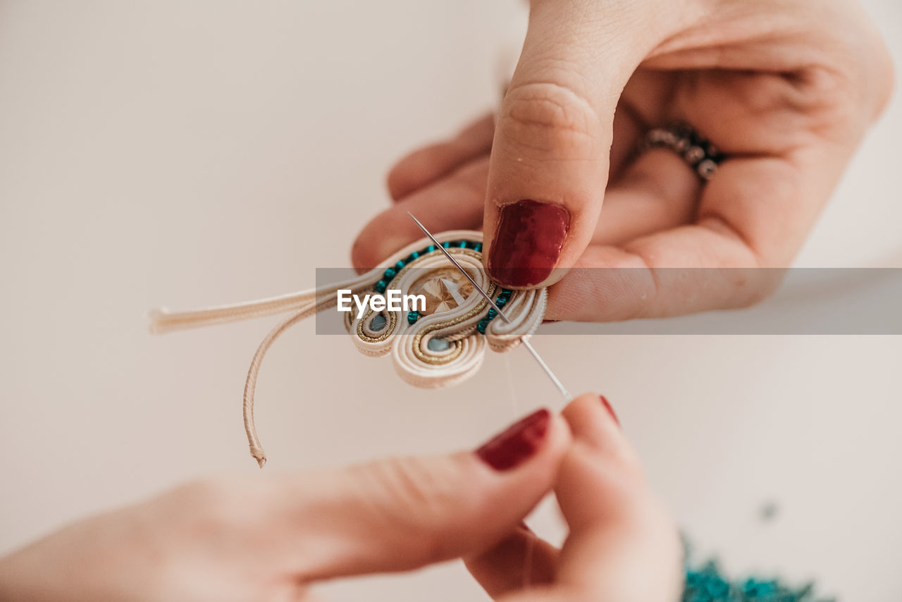 Closeup of crop skilled craftswoman creating soutache bijouterie with threads and beads in bright workshop