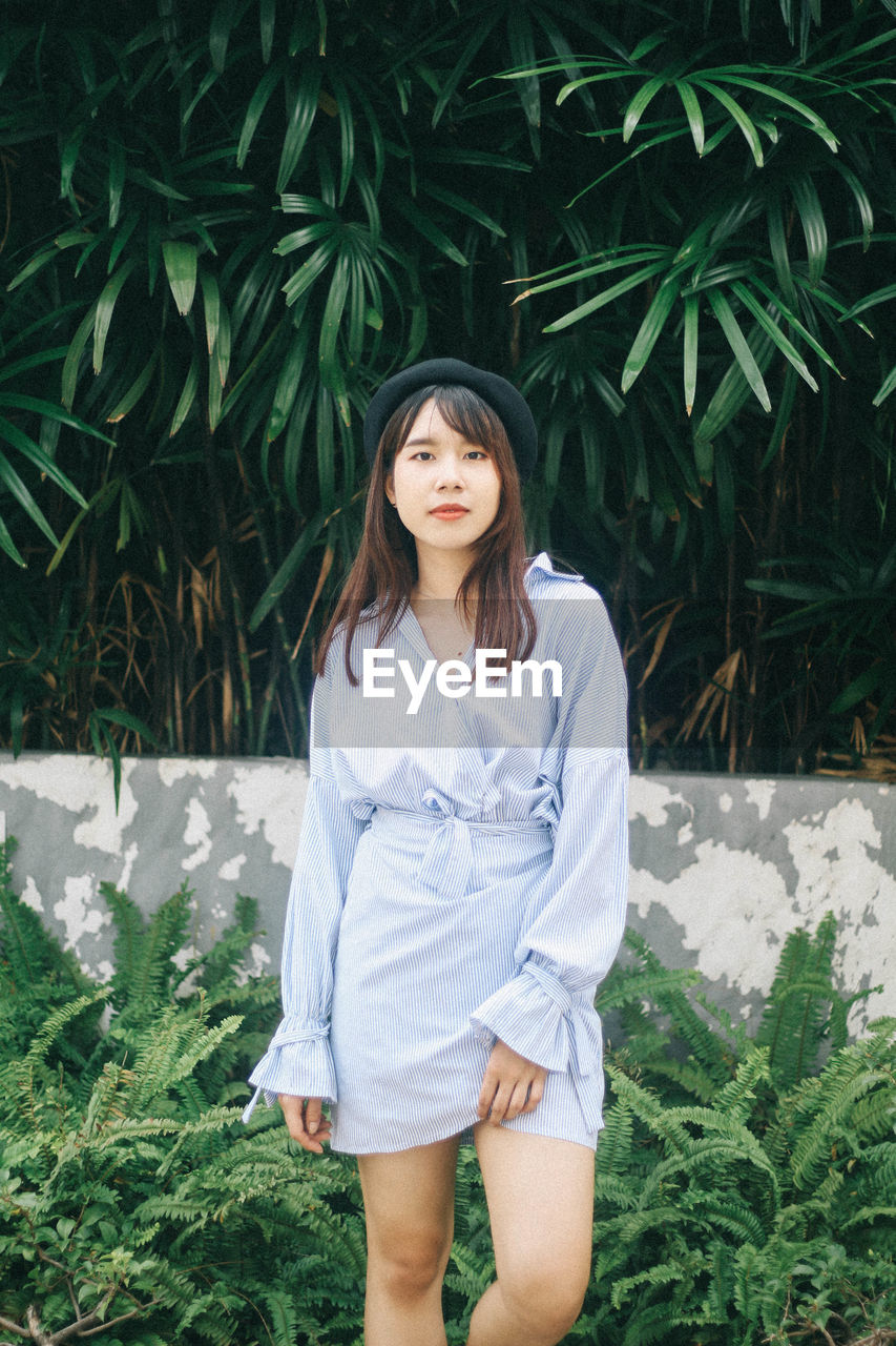 Portrait of beautiful young woman standing against plants