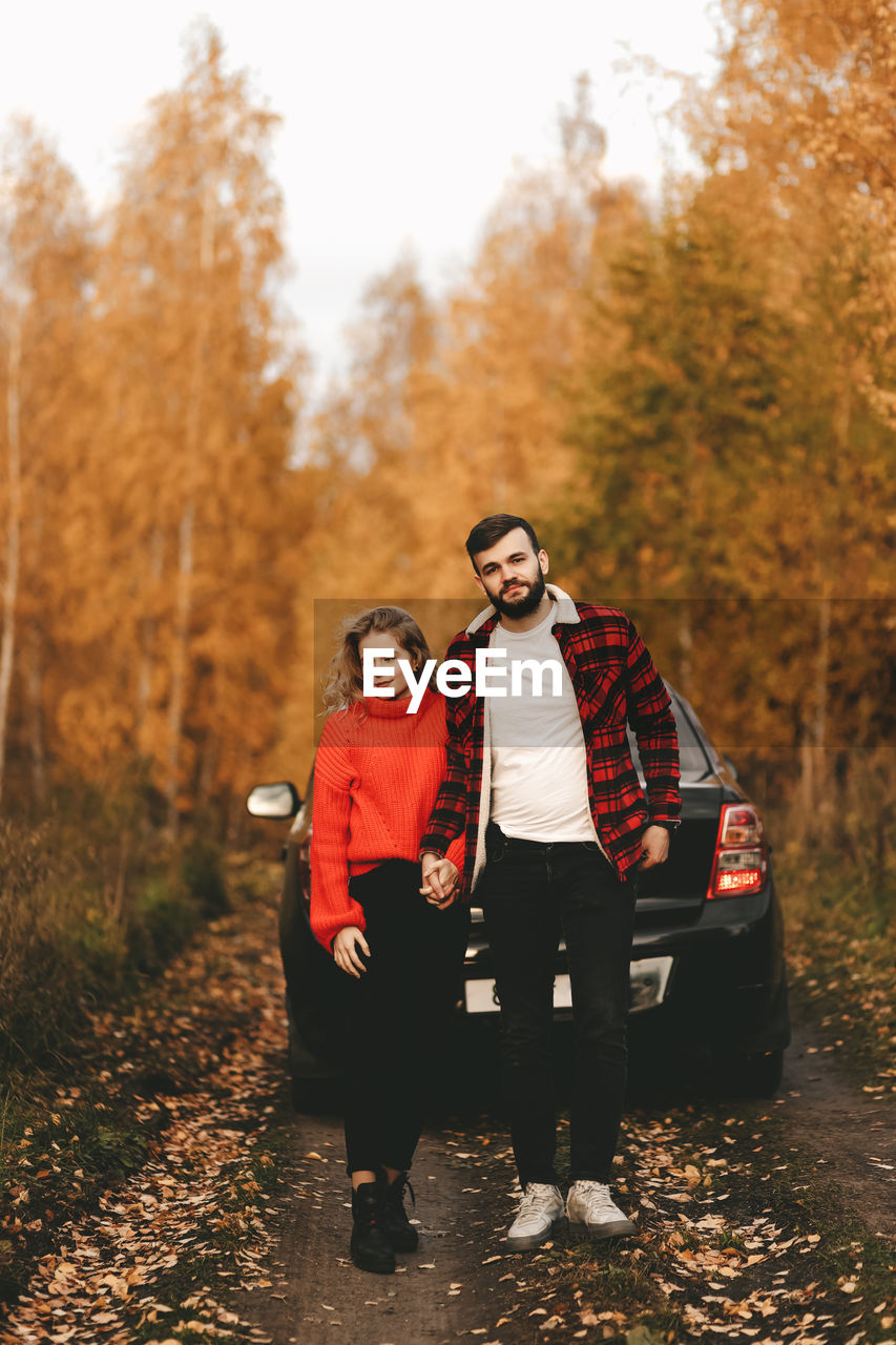 A romantic couple in love in warm sweaters is walking traveling by car in the autumn forest in fall