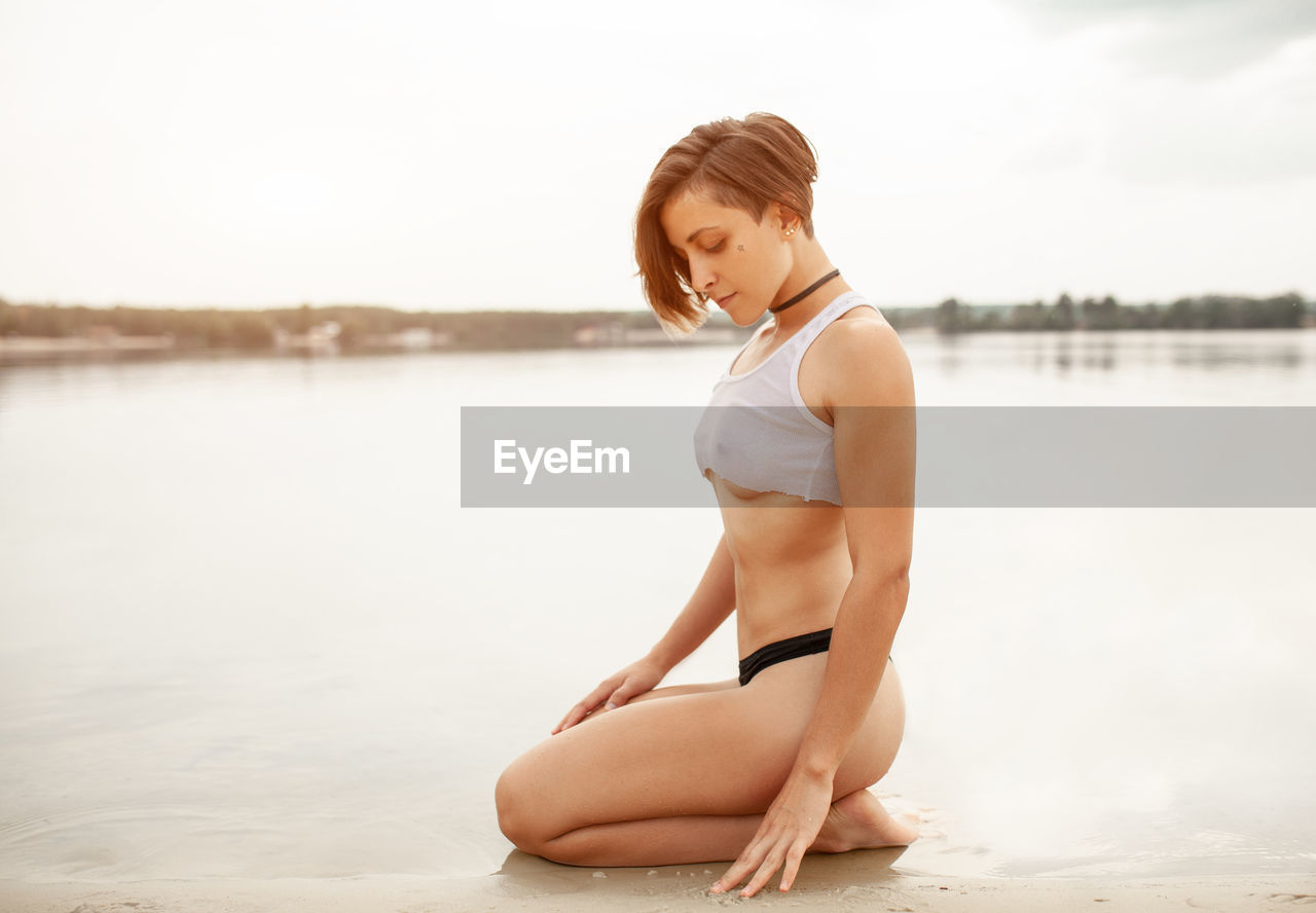 Side view of sensuous young woman at beach against sky