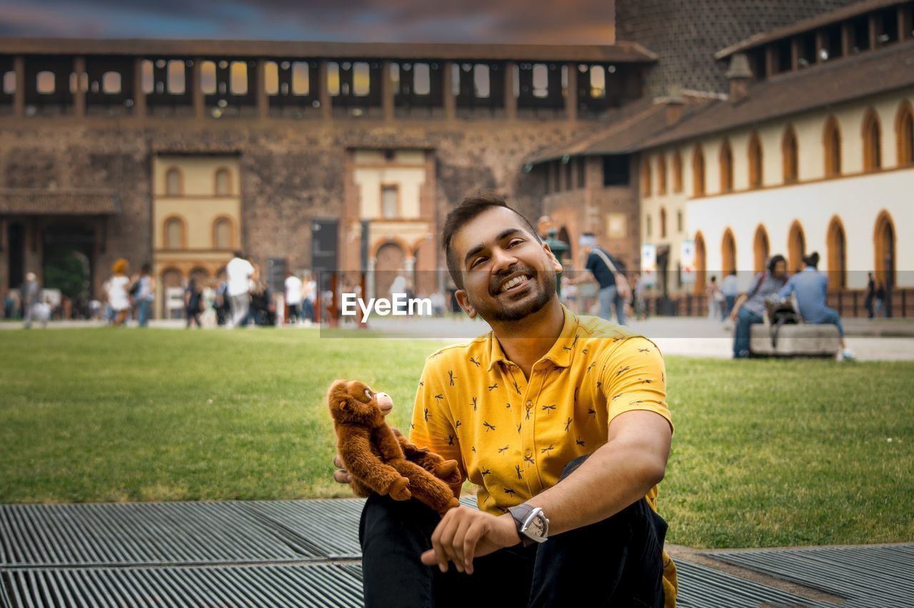 Portrait of cheerful young man holding toy animal while sitting against building