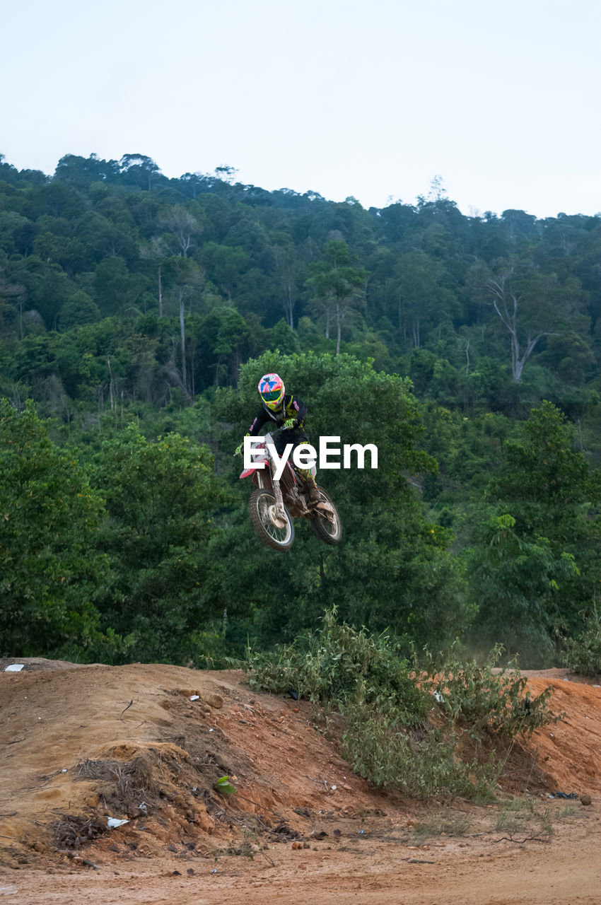Man performing stunt with motorbike against trees