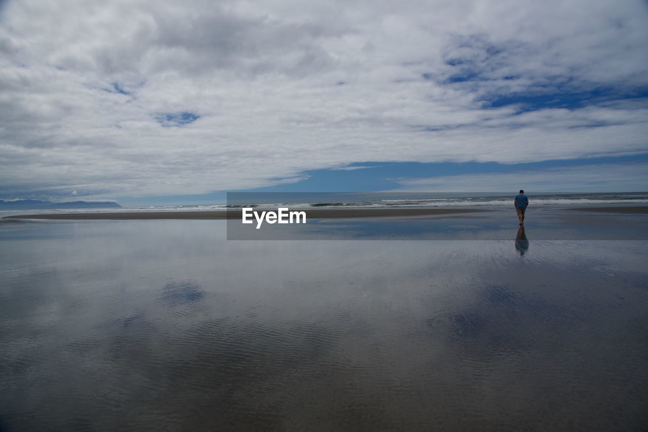 Man walking on shore at beach against sky