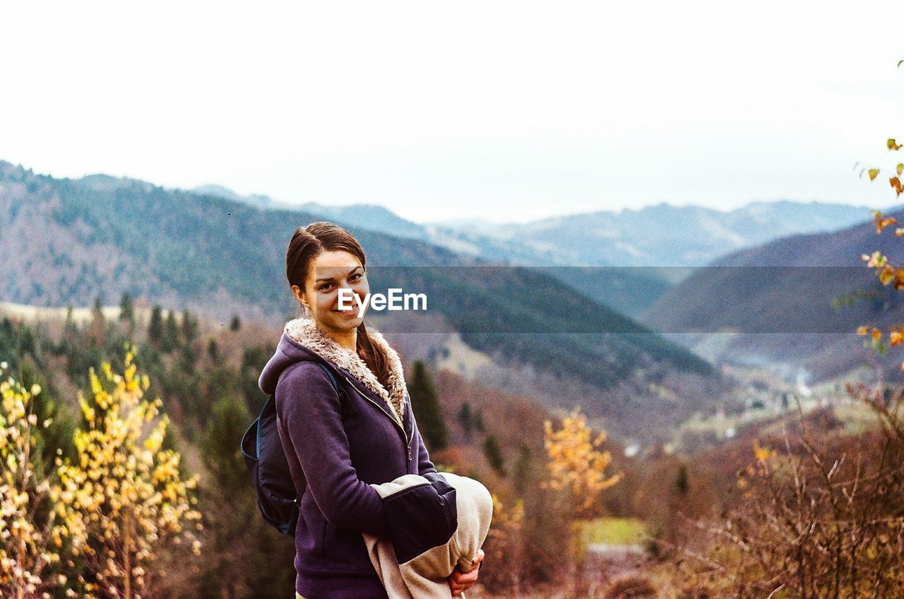 Portrait of smiling young woman standing against mountain range