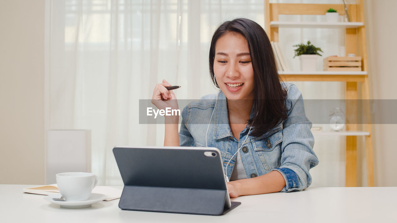 Smiling young woman video conferencing over digital tablet on table at home