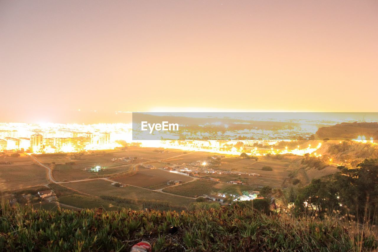 HIGH ANGLE VIEW OF ILLUMINATED CITYSCAPE AGAINST SKY DURING SUNSET