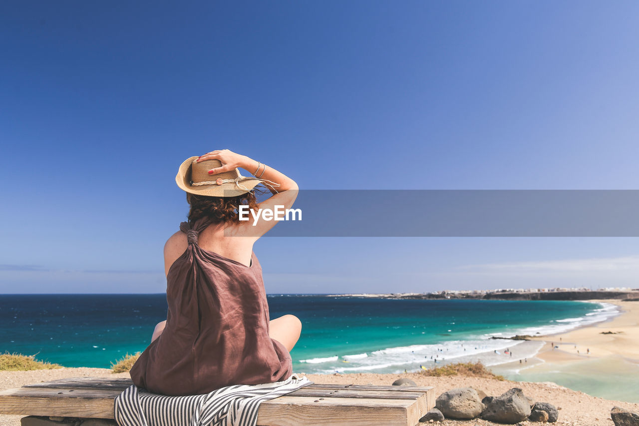 Woman sitting on bench at beach against clear sky