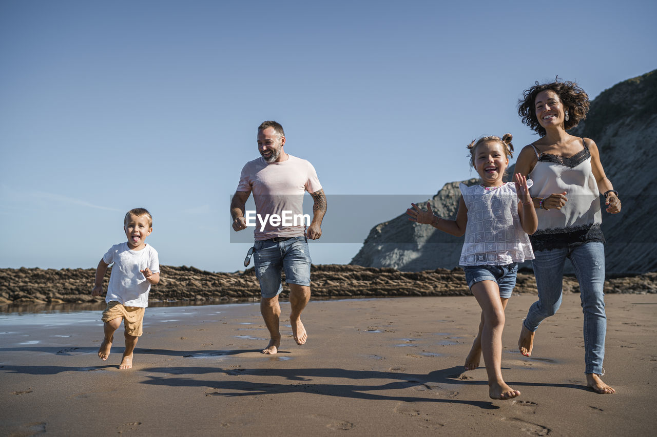 Family having fun while running on beach against sky