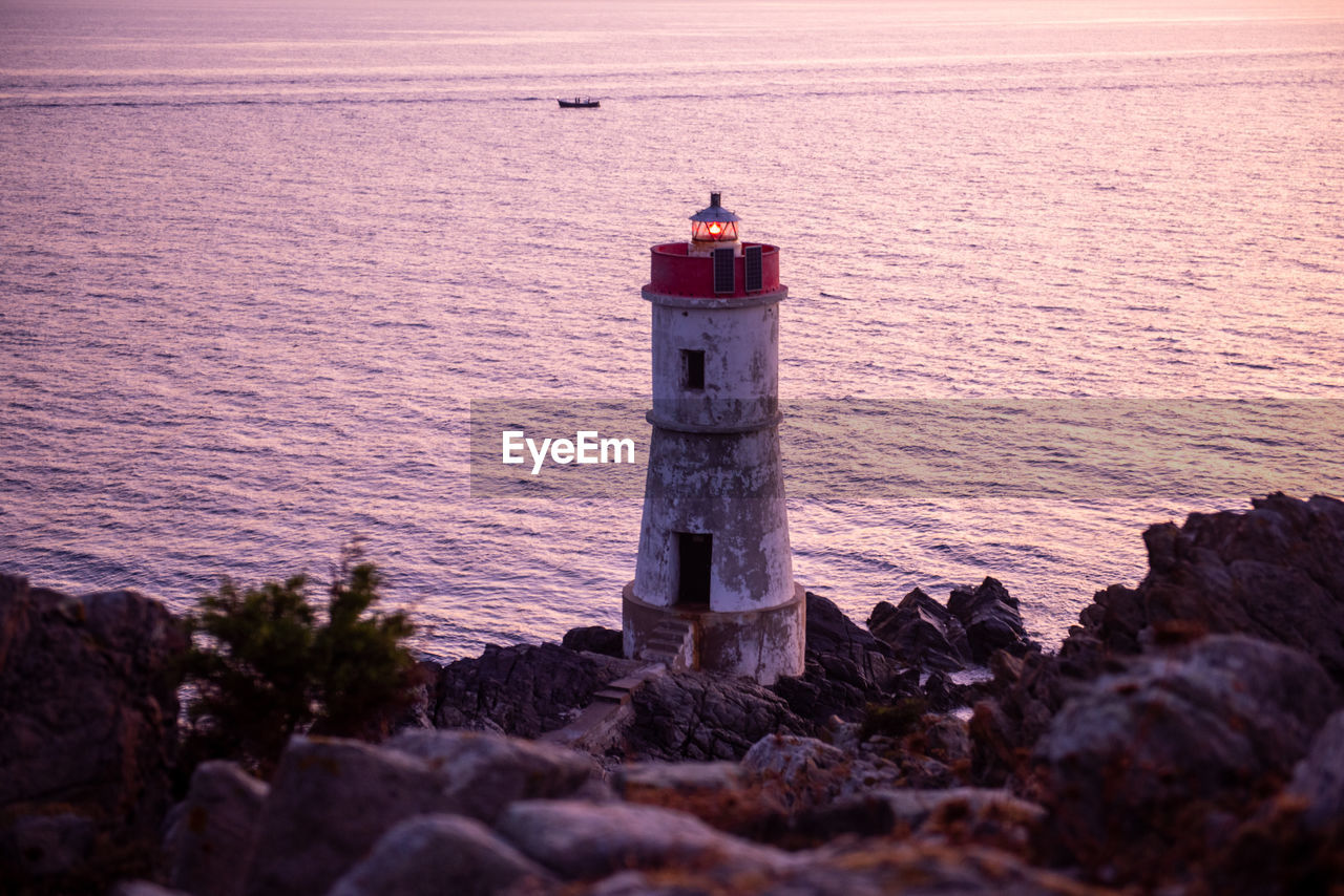 Lighthouse on rock by sea against sky