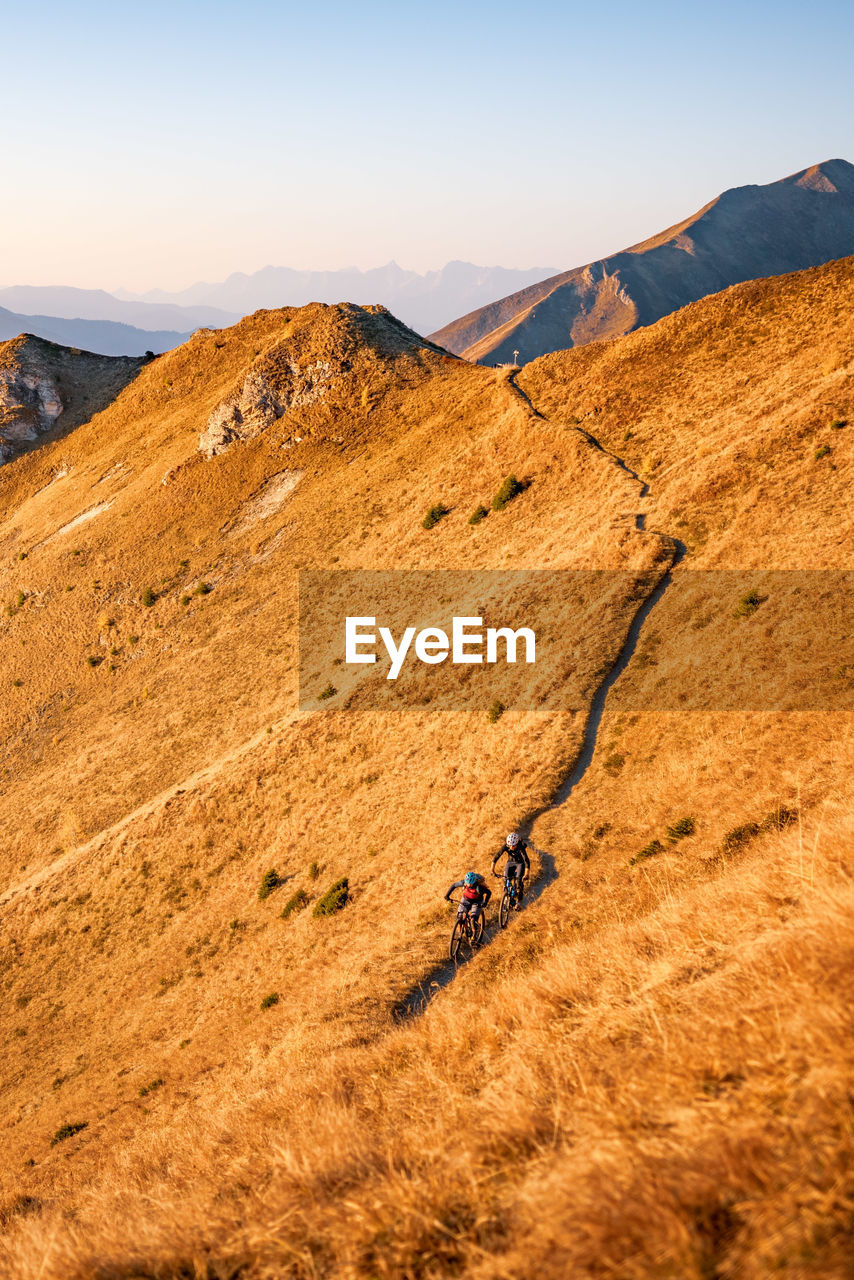 Men cycling on mountain road against sky