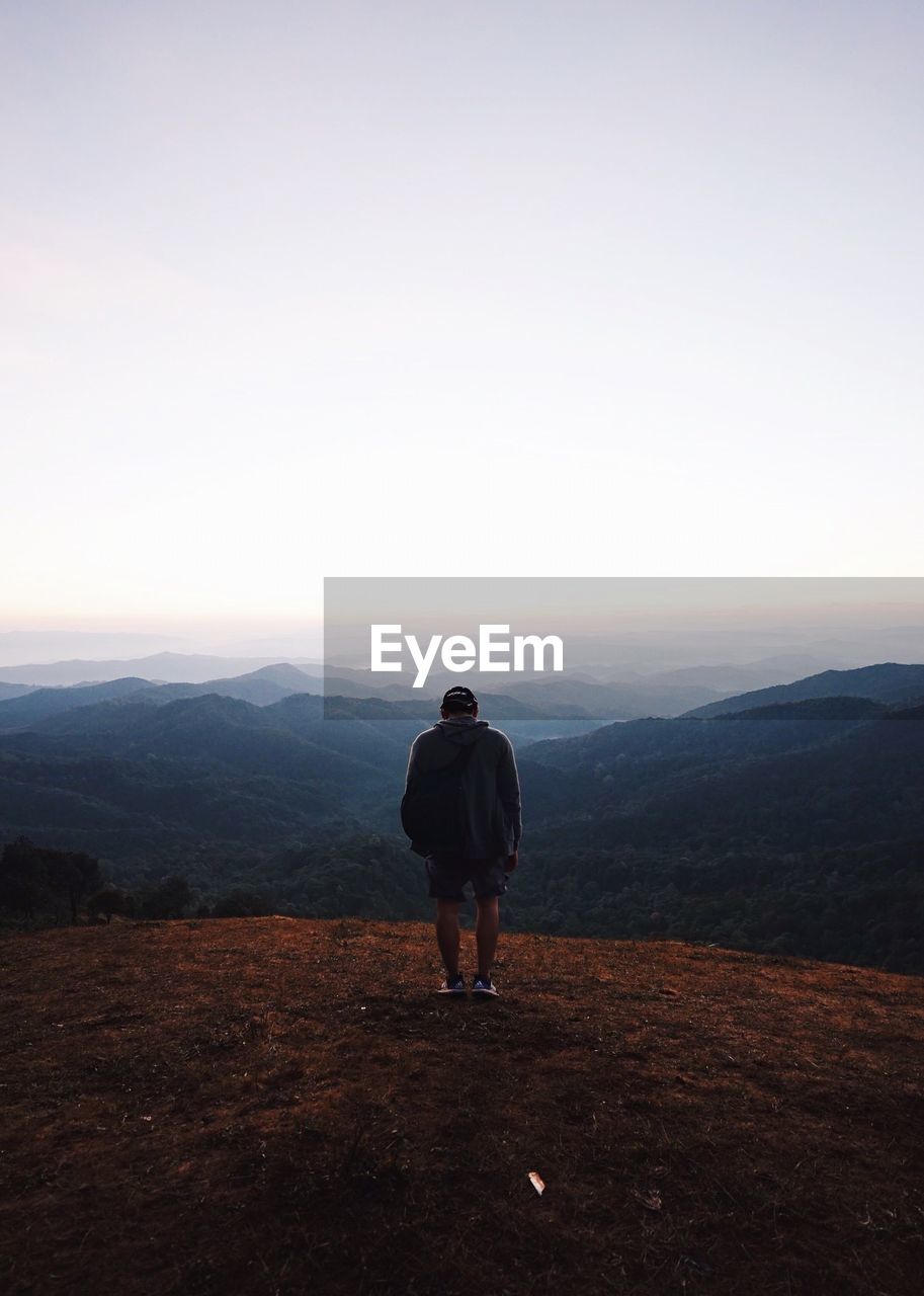 Rear view of man standing on mountain against clear sky