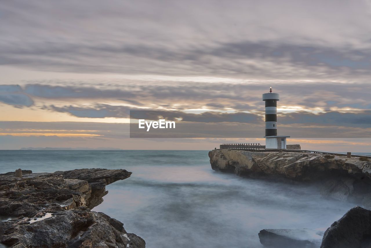 Lighthouse by sea against sky during sunset