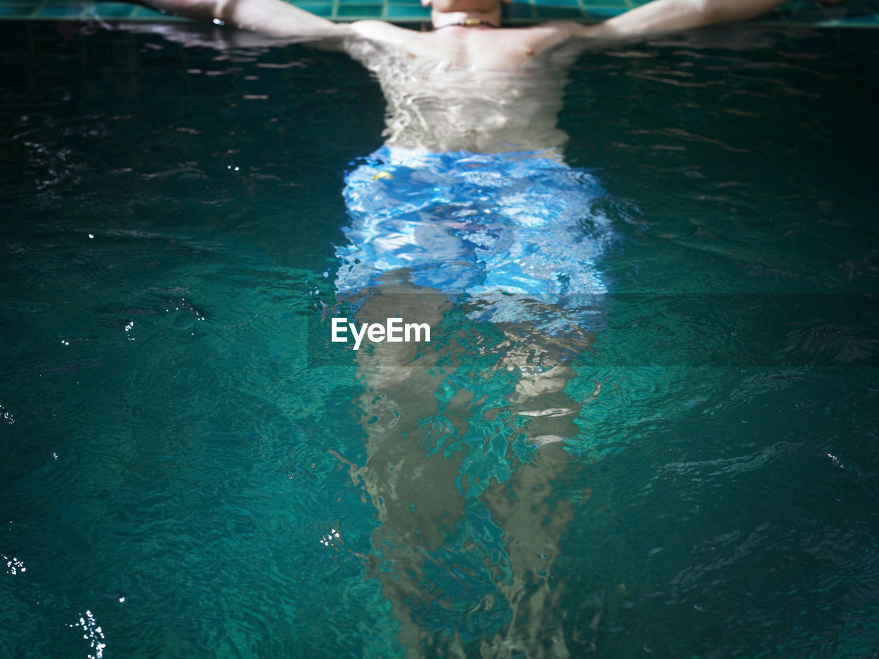 Low section of shirtless young man swimming in pool