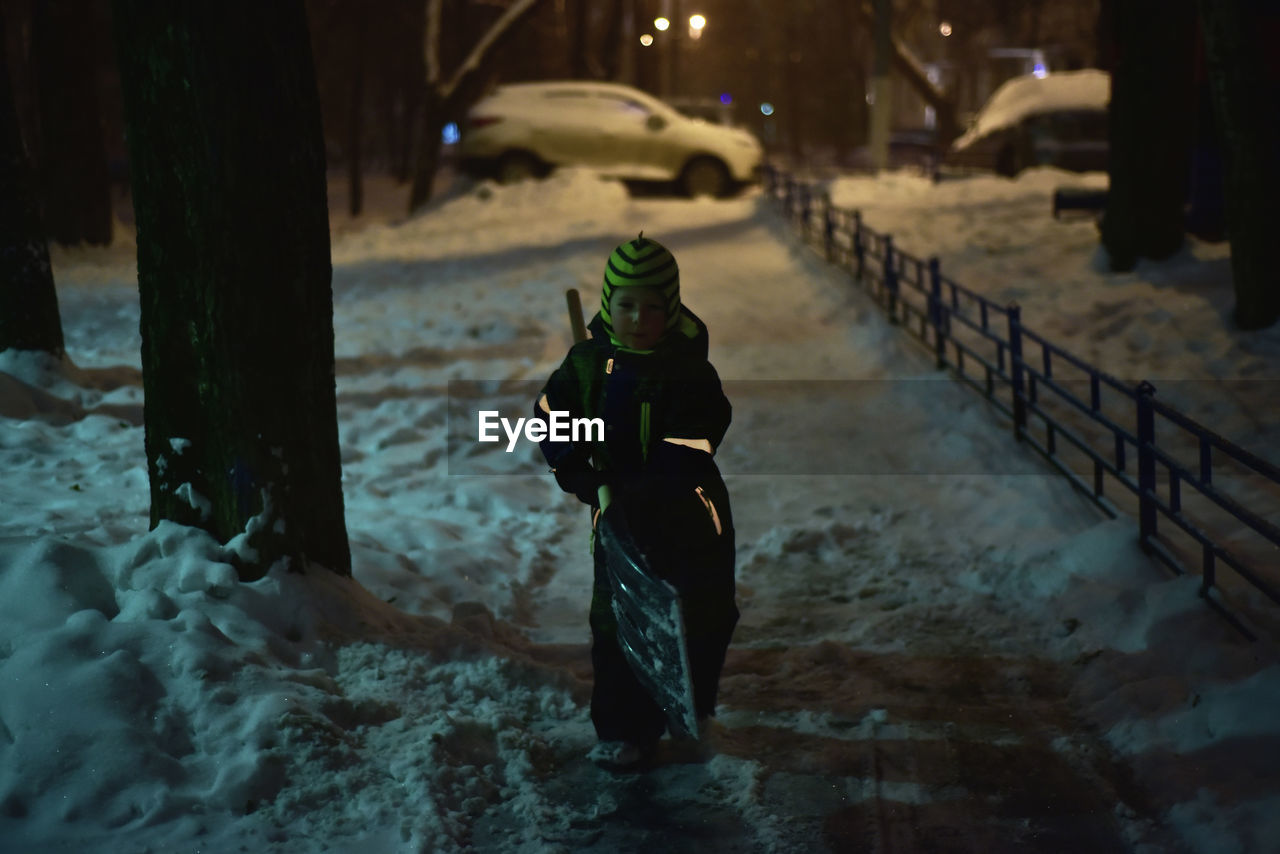 Portrait of boy cleaning snow at night