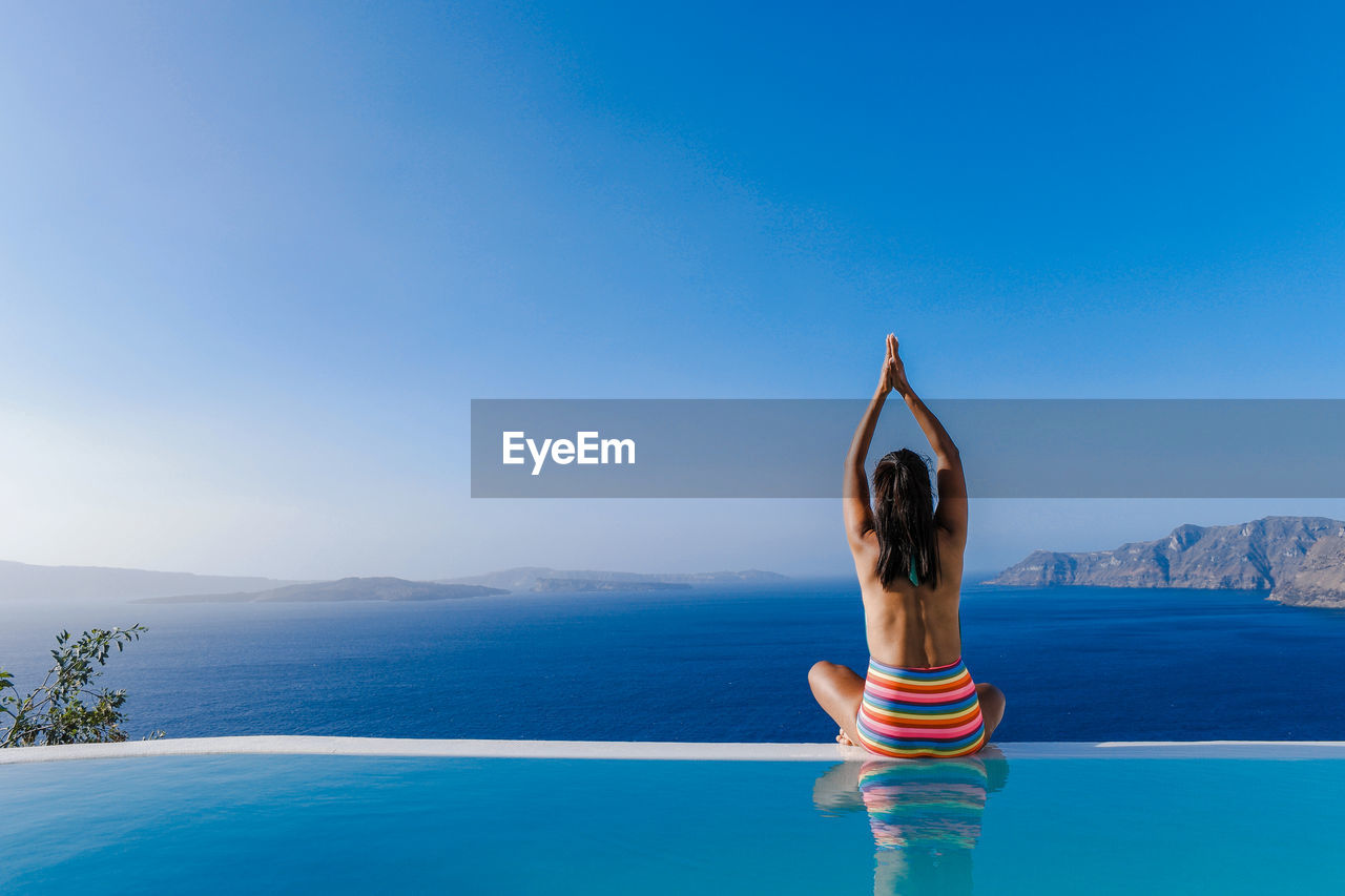 Woman practicing yoga in swimming pool against sea