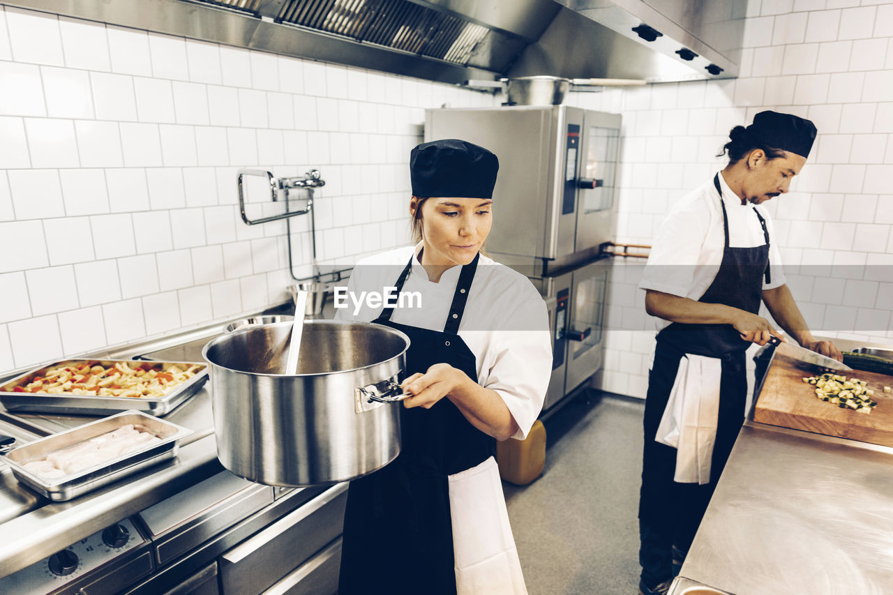 Kvinnlig kock bär på gryta i restaurangkök