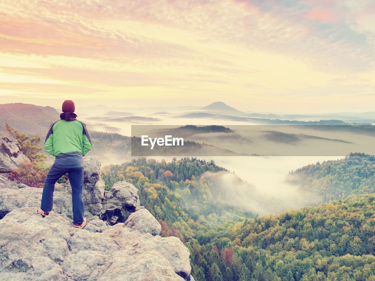 Man stay on rocky peak within daybreak and watch over misty landscape. beautiful autumn morning.