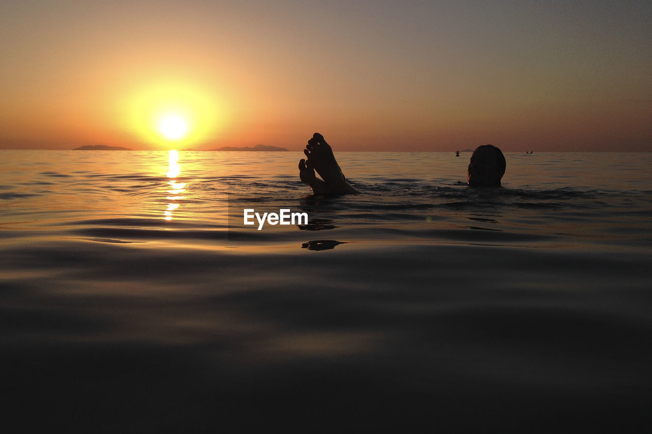 SILHOUETTE MAN SWIMMING IN SEA AT SUNSET