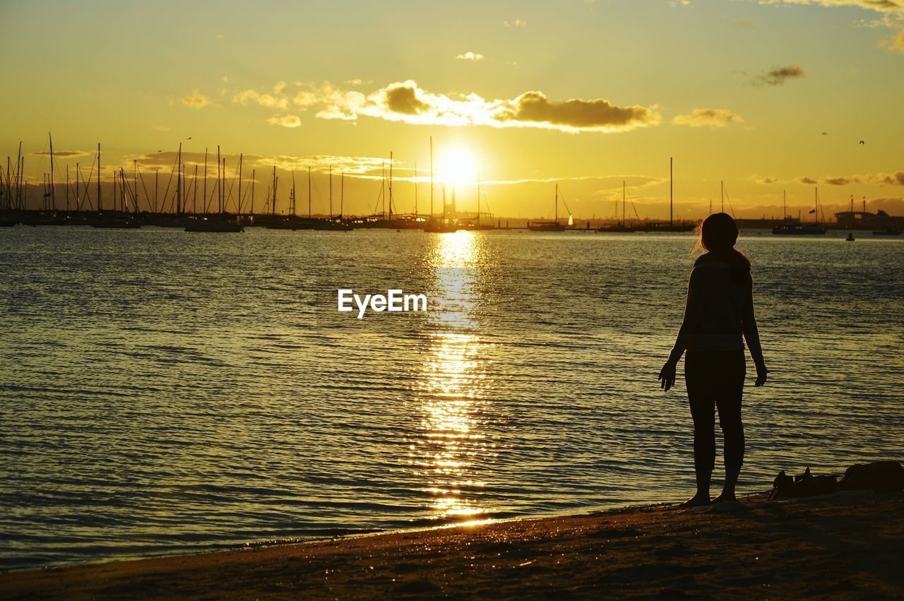 Rear view of silhouette woman standing at st kilda beach during sunset