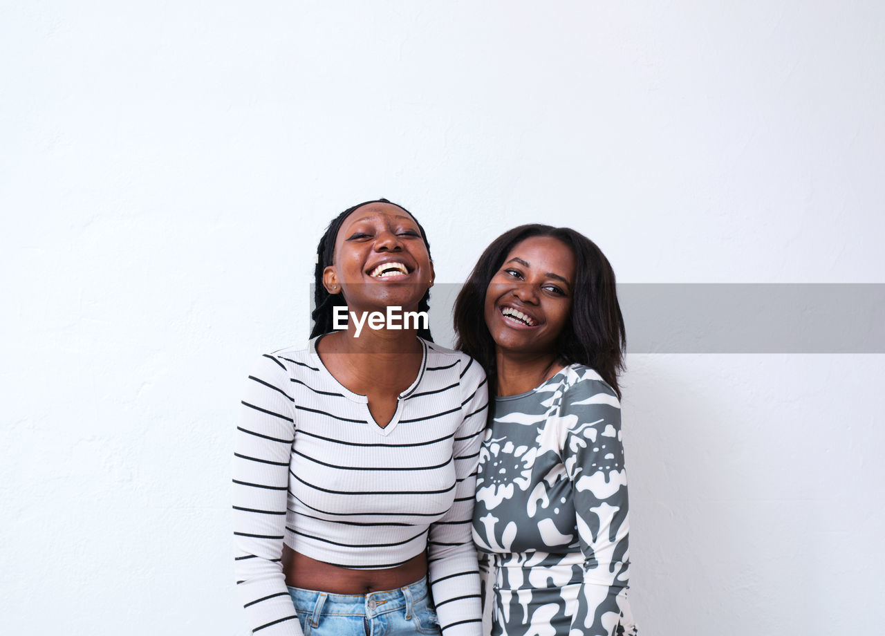 Cheerful african american females in casual clothes hugging and laughing in studio against white background